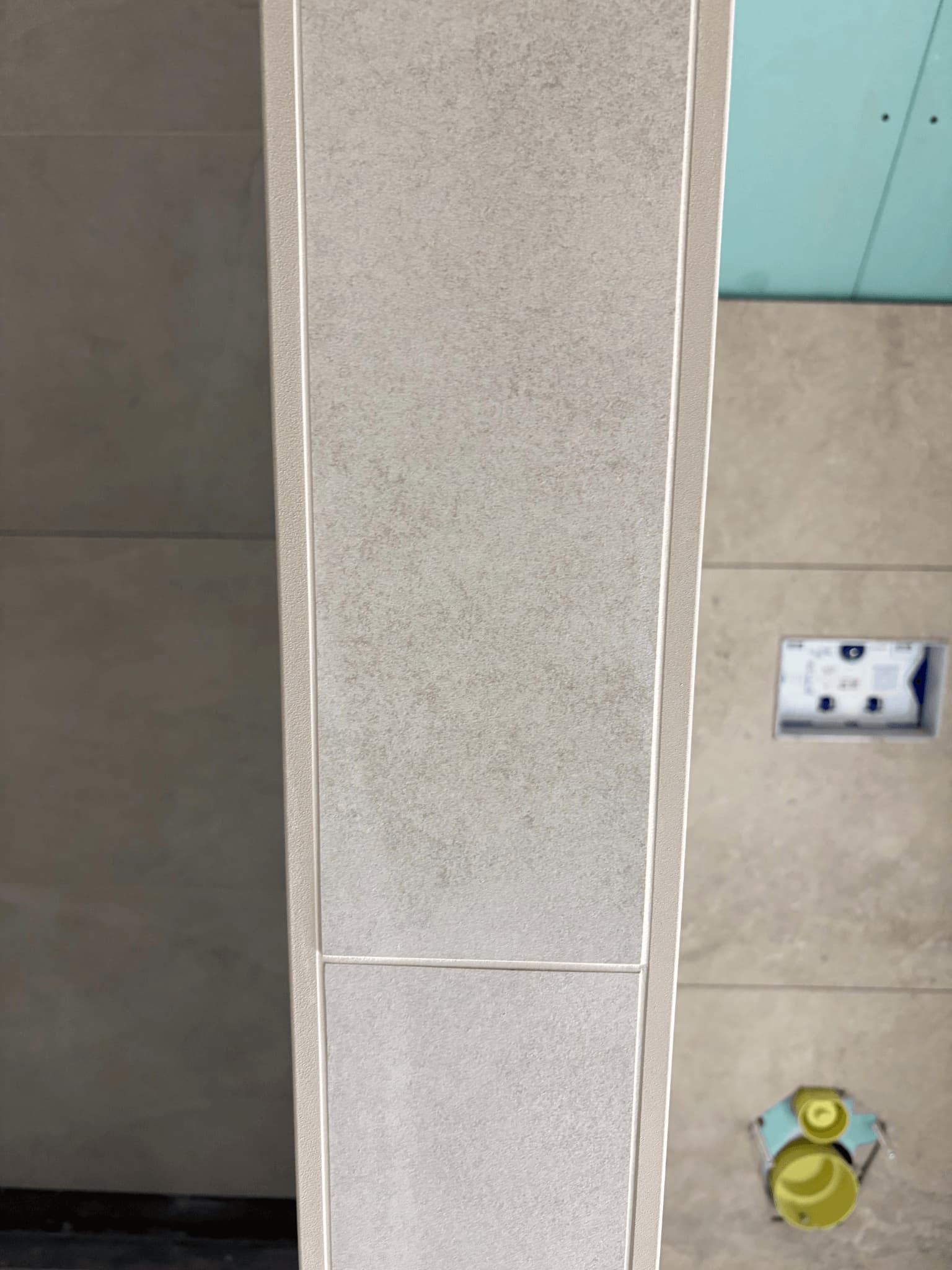 Close-up van een sierstrip tussen wandtegels, met strak afgewerkte voegen.